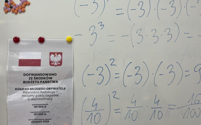 Plakat informacyjny „Dofinansowano ze środków budżetu państwa – Kompas Młodego Obywatela, Przenośna Redakcja” przypięty magnesami do tablicy, obok działania na potęgach z lekcji matematyki