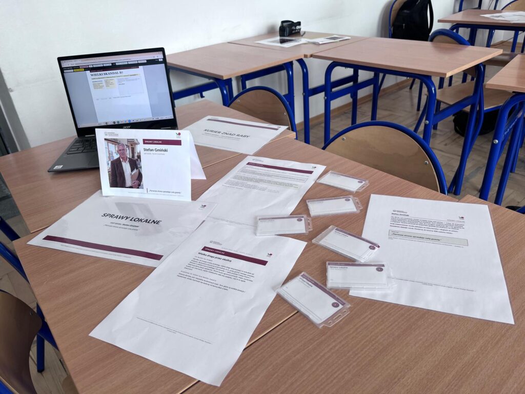 Stolik działu Sprawy lokalne przed warsztatem: laptop, karta szefa działu, identyfikatory i karty zadań