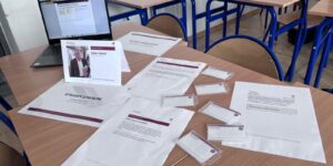 Stolik działu Sprawy lokalne przed warsztatem: laptop, karta szefa działu, identyfikatory i karty zadań