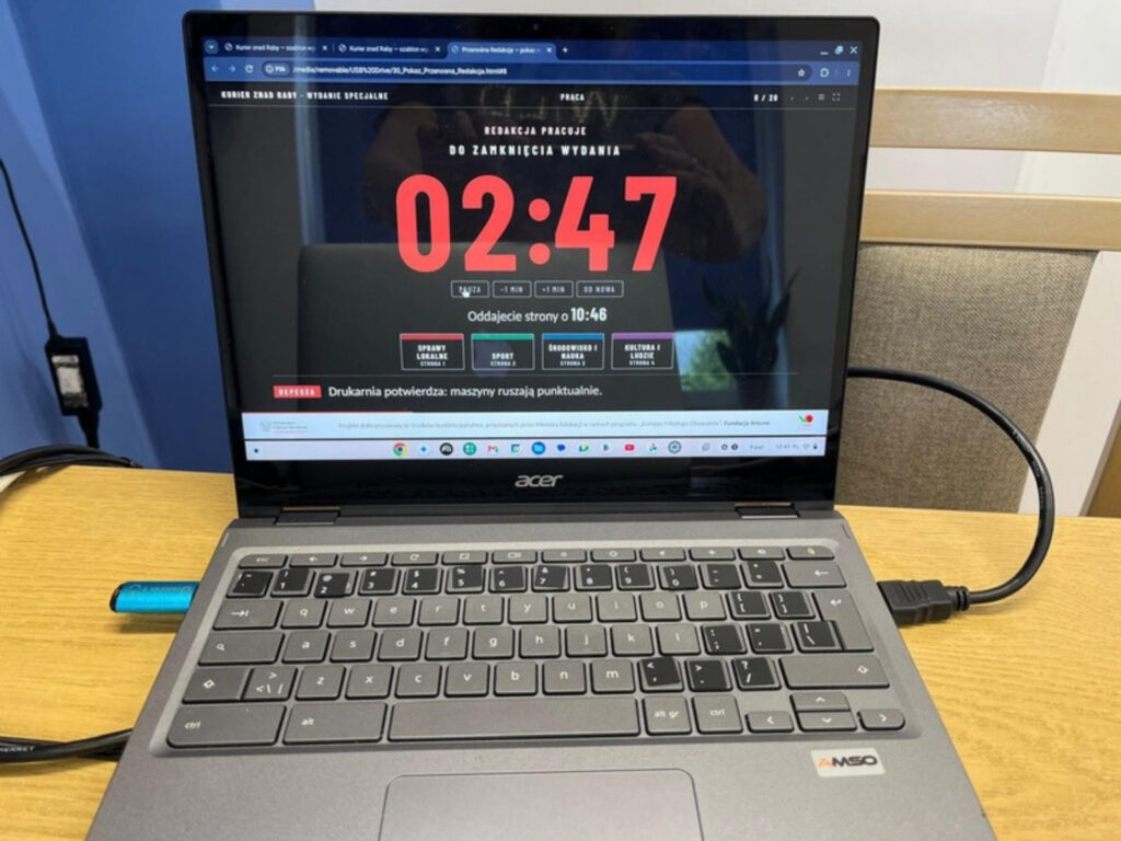 Laptop z zegarem redakcji: „Do zamknięcia wydania 02:47”, „Oddajecie strony o 10:46”, cztery działy gazety i depesza „Drukarnia potwierdza: maszyny ruszają punktualnie”