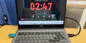 Laptop z zegarem redakcji: „Do zamknięcia wydania 02:47”, „Oddajecie strony o 10:46”, cztery działy gazety i depesza „Drukarnia potwierdza: maszyny ruszają punktualnie”